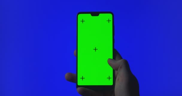 Telefone na mão fechar isolado em fundo azul. A tela do telefone é a chave azul do chroma, tela verde da chave do croma do fundo. Filmagem para anúncios móveis, app promo — Vídeo de Stock