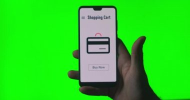 İnternetten satın alma ve ödemeyle ilgili ekranda animasyonu olan birinin elinde bir cep telefonu. Buy Now düğmesine tıklayın. İnternet bankacılığı yoluyla para göndermek. Kromakey için yeşil arkaplan.