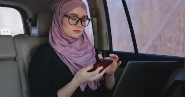 A Muslim business woman rides in a car and looks at papers and talks on the phone. Conduct business remotely from your car. Business woman. — Stock Video