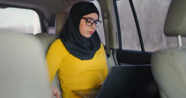 Een moslim zakenvrouw rijdt in een auto en kijkt naar papieren en praat aan de telefoon. Doe zaken op afstand vanuit je auto. Zakelijke vrouw. — Stockvideo