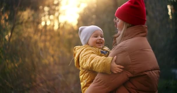 Linsenblitz in Zeitlupe: Junge Mutter und Sohn in gelber Jacke im Park träumen, umarmen sich liebevoll und verbringen Zeit miteinander. Glückliche Kindheit. Zeit mit der Familie in der Natur verbringen. — Stockvideo