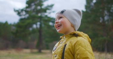 Yavaş çekim mutlu çocuk yakından gülüyor ve hayalperest Park 'ın ve ağaçların doğasına bakıyor. Etrafındaki dünyayı bilen bir çocuk. Tatmin olmuş ve ormandaki bebeğe hayran kalmış..