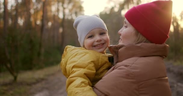 I solljuset i slow motion kramar mamma och kysser sin son. Ta hand om ett 2-3-årigt barn. Promenad på hösten och våren park. Mödradagen. — Stockvideo