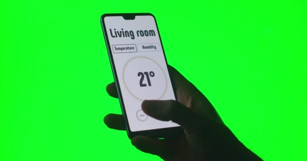 Kromakeyin yeşil arka planında bir adam cep telefonundaki bir uygulama aracılığıyla sıcaklık ve alarm sistemlerini kontrol eder. — Stok video
