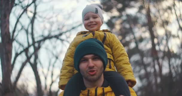 Loving young dad carrying cute little kid son giving piggyback ride in woodland, happy funny small boy sitting on father shoulder playing carrying child bonding having fun laughing in park — Stock Video