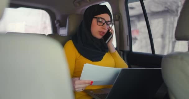 A Muslim business woman rides in a car and looks at papers and talks on the phone. Conduct business remotely from your car. Business woman. — Stock Video