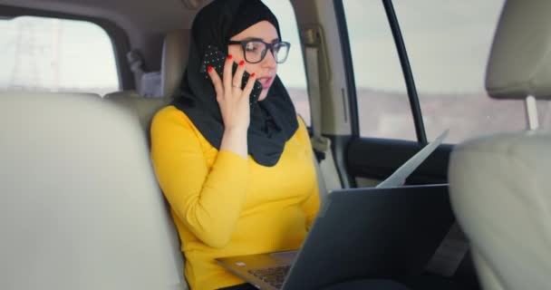 Une femme d'affaires musulmane monte dans une voiture et regarde les papiers et parle au téléphone. Faites des affaires à distance depuis votre voiture. Femme d'affaires . — Video