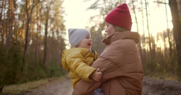 Lencse fellobban lassított felvételen: Fiatal anya és fia sárga kabátban a parkban álmodoznak és szeretnek ölelkezni és együtt lenni. Boldog gyerekkort. A családdal töltött idő a természetben. — Stock videók