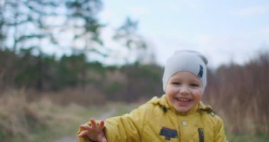 Yavaş çekim mutlu çocuk yakından gülüyor ve hayalperest Park 'ın ve ağaçların doğasına bakıyor. Etrafındaki dünyayı bilen bir çocuk. Tatmin olmuş ve ormandaki bebeğe hayran kalmış..