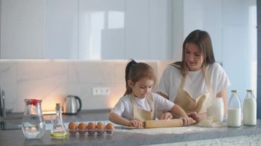 Kız ve anne evde, mutfakta önlüklerle un dökerek merdaneyle rulo yapıp hamuru elleriyle yontuyorlar. Çocuklarla vakit geçir ve tecrübelerini paylaş..