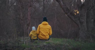 Parkta kütüğün üzerinde otururken oğlunu kucaklayan mutlu bir baba. Odunların üzerinde oturup kameraya bakarken mutlu baba oğlunu kucaklıyor. Yavaş çekim değerli anlar, baba ve oğulun yakınlığı.