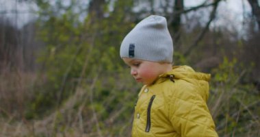 Aktif bir çocuk ormanda yürüyor. Autumn Park 'ta sarı yapraklı bir çocuğa yakın çekim. Bir çocuk ormandaki sarı yaprakların arasından geçer. Yavaş çekim