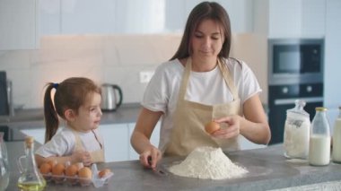 Evde, mutfakta, anne ve kız bir yumurta kırar ve kek için una süt eklerler. Ev yemeği, makarna ve pizza.