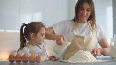 Evde, mutfakta, anne ve kız bir yumurta kırar ve kek için una süt eklerler. Ev yemeği, makarna ve pizza.