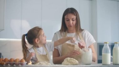 Kız ve anne evde, mutfakta önlüklerle un dökerek merdaneyle rulo yapıp hamuru elleriyle yontuyorlar. Çocuklarla vakit geçir ve tecrübelerini paylaş..