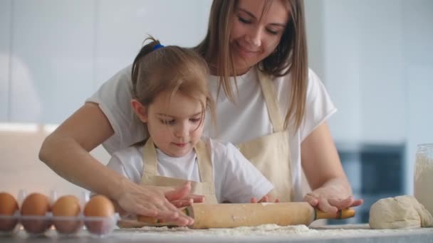 Kız ve anne evde, mutfakta önlüklerle un dökerek merdaneyle rulo yapıp hamuru elleriyle yontuyorlar. Çocuklarla vakit geçir ve tecrübelerini paylaş.. — Stok video