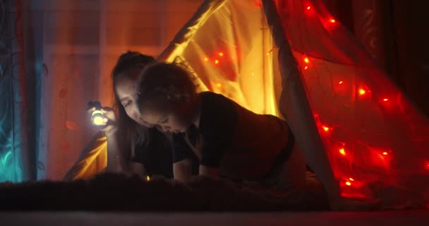 História para dormir. Mãe feliz e filho pequeno leram um livro em uma tenda em casa. Lendo um livro sob um cobertor com uma lanterna em um quarto escuro à noite. Mulher caucasiana desfrutando de tempo em família com seu filho . — Vídeo de Stock