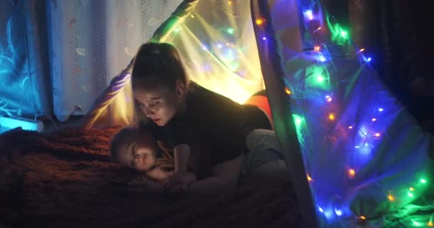 Cuento para dormir. Madre feliz e hijo pequeño leyeron un libro en una tienda de campaña en casa. Leyendo un libro bajo una manta con una linterna en una habitación oscura por la noche. Mujer caucásica disfrutando de tiempo en familia con su hijo . — Vídeos de Stock