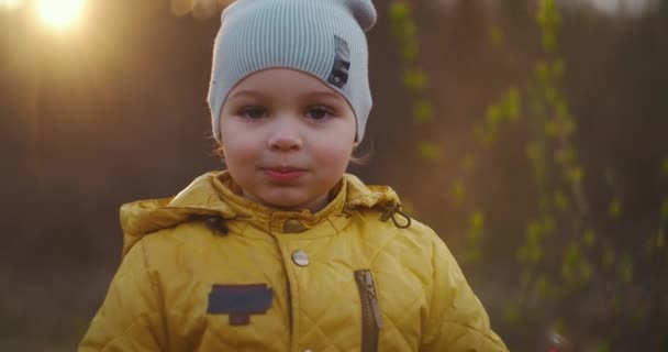 Медленное движение: Мальчик в желтой куртке Исследуйте мир вокруг него, сидя в лесу на солнце. Наслаждайтесь и смейтесь в лесу. Бесплатное веселое детство в парке на природе — стоковое видео