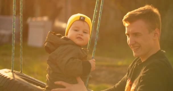 Glad pappa rullar en glad son på en gunga i en park på en ek träd. Begreppet lycklig familj. Ensamstående far. Slow motion far och son på en swing på fars dag. — Stockvideo