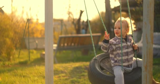 Молодий хлопчик катається на гойдалках у повільному русі на сонці. Світло від сонця входить у камеру . — стокове відео