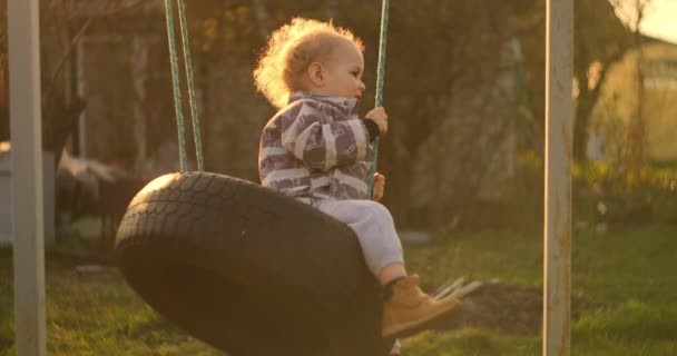 Mladý chlapec jezdí na houpačce ve zpomaleném pohybu na slunci. Světlo ze slunce vstupuje do kamery. — Stock video