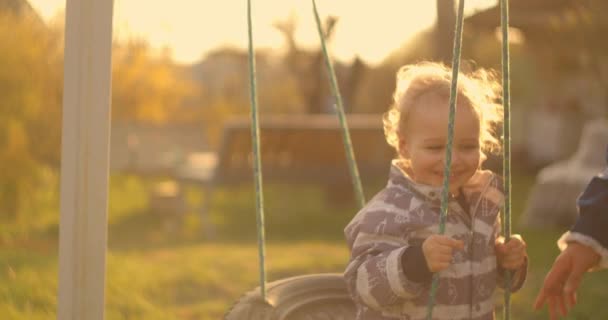 若い男の子は太陽の下でゆっくりとした動きでスイングに乗る。太陽からの光がカメラに入る. — ストック動画