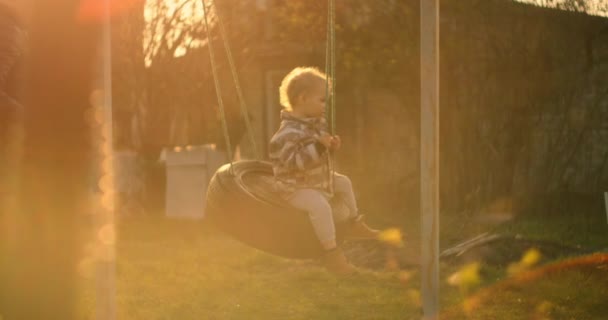 Młody chłopiec jeździ na huśtawce w zwolnionym tempie na słońcu. Światło od słońca wchodzi do kamery.. — Wideo stockowe