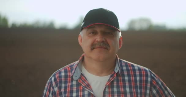 Portrait of the thoughtful senior farmer looks at camera. Senior Farmer smiling. Slow motion. Close up of the Caucasian good looking young man with a beard smiling to the camera — Stock Video