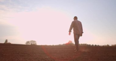 Çiftçi gün batımında tarlada tarlada yürüyor. Çiftçi gün batımında tarlada yürürken alnındaki teri siliyor. İş için lastik botlar. Bir işçi gün batımında lastik botlarla gider.