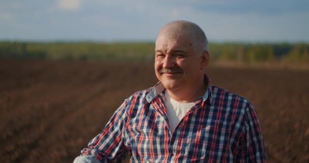 Ağır çekim: Kafkasyalı yakışıklı, şapkalı bilge bir çiftçinin yanına yaklaş, yüzünü kameraya çevir ve buğday tarlasında gülümse. Portre — Stok video