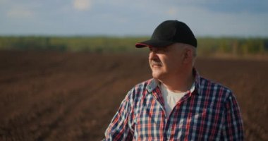 Ağır çekim: Kafkasyalı yakışıklı, şapkalı bilge bir çiftçinin yanına yaklaş, yüzünü kameraya çevir ve buğday tarlasında gülümse. Portre