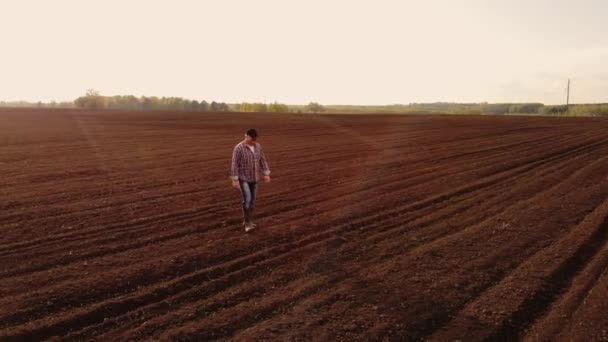 Fotografia aérea o drone segue um fazendeiro caminhando através de um campo arado com terra. Voar ao redor e seguir os agricultores vista superior — Vídeo de Stock