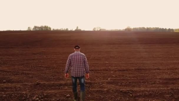 Vista aérea del granjero caminando por sus campos. Un granjero adulto con gorra camina a través de un campo arado y con cultivos plantados en sus botas. Vista superior de un hombre inspeccionando los campos. Agricultor . — Vídeo de stock