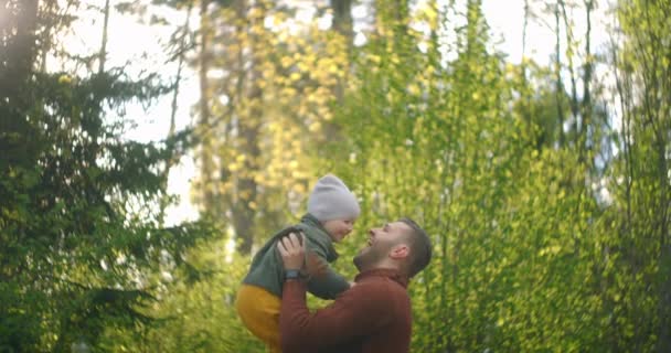 Zeitlupe: Vater wirft seinen Sohn nach draußen. Vater und Sohn spielen und genießen den Sonnenuntergang im Weizenfeld in der Natur. Kleiner Junge und Vater haben Spaß dabei, Sohn in die Luft zu werfen. — Stockvideo