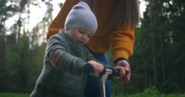 Anne ve oğlu dışarıda scooter kullanıyor. Bizi her zaman gururlandırır. Küçük şirin bir çocuk mini scooter 'a biniyor, parkta ağır çekimde scooterı tekmeliyor. Annem scooter sürmeyi öğretiyor.