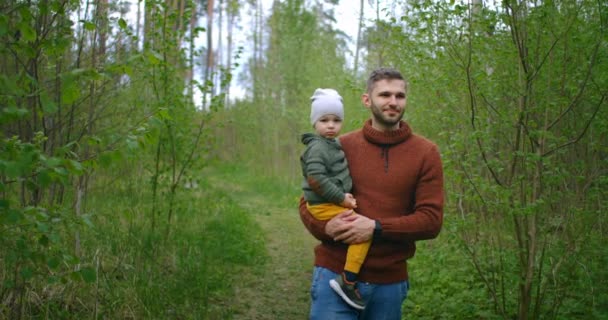 Gün batımında parkta yürüyen baba ve oğul. İki yaşında bir çocuk ebeveyn omuzlarında oturuyor. Mutlu aile kavramı. Baba oğlunu omuzlarında taşıyor.. — Stok video