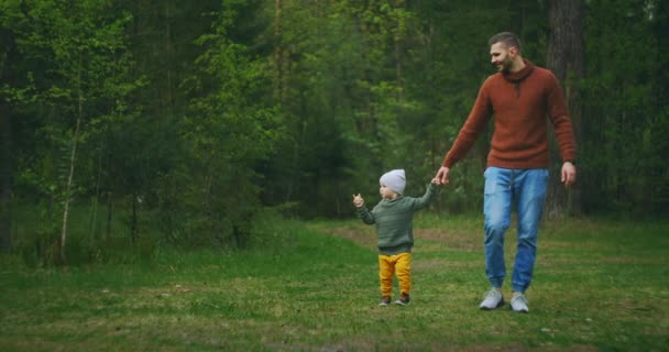 スローモーション:ハンサムな若い男と彼のかわいい息子は森の中を歩いていて、新鮮な空気、自然、コミュニケーションを楽しんでいます。家族、父と観光の概念 — ストック動画