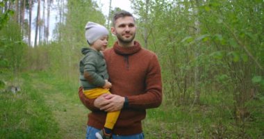 Yavaş çekim: Yakışıklı genç adam ve sevimli küçük oğlu ormanda yürüyor ve temiz havanın, doğanın ve iletişimin tadını çıkarıyorlar. Aile, babalık ve turizm konsepti