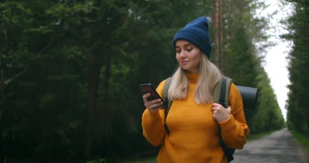 Flicka med ryggsäck Använda smartphone Gps. Kvinna vandring i skogen och skriva meddelande på smartphone. Solo kvinnliga vandrare med hjälp av smarttelefon. Kvinnlig vandrare tar smart telefon bild av berg och skog. — Stockvideo