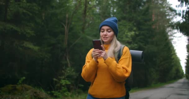 Flicka med ryggsäck Använda smartphone Gps. Kvinna vandring i skogen och skriva meddelande på smartphone. Solo kvinnliga vandrare med hjälp av smarttelefon. Kvinnlig vandrare tar smart telefon bild av berg och skog. — Stockvideo