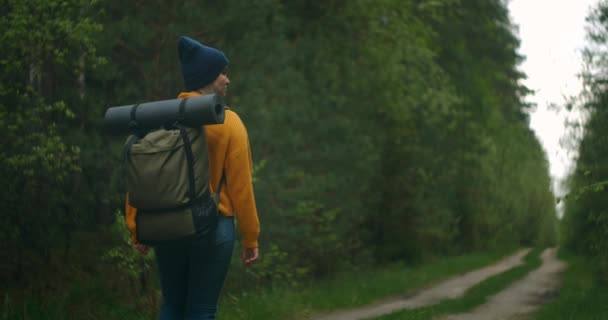 慢动作：秋天在森林中远足的年轻女子。一个积极健康的白人女人背着背包带着木头沿着森林后视镜、休闲、生物旅游、远足的女游客 — 图库视频影像