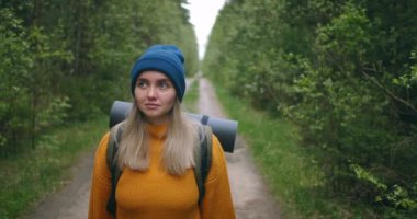 Yavaş hareket eden kadın yürüyüşçü ormanda levada patikası boyunca yürüyor. Mutlu sırt çantalı bayan doğa hayranı kırsal yolda yürüyor. Güneşli bir sonbahar gününde, sonbahar ormanında yürüyen bir kadın turist..