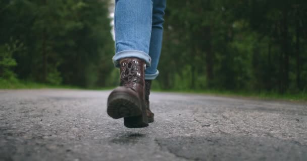 Zbliżenie stóp w butach w zwolnionym tempie spacerujących po asfaltowej drodze. Autostopem. Podróżująca kobieta — Wideo stockowe