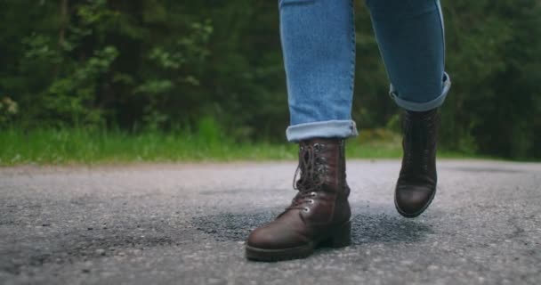 Detailní záběr nohou ve zpomalených botách kráčejících po asfaltové cestě. Stopem. Žena cestovatelka — Stock video
