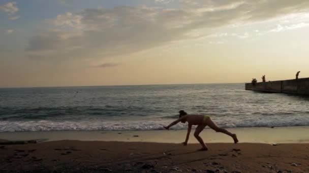 A kislány ezzel cigánykerék a tengerparton a gyönyörű naplementét. Sziluettjét — Stock videók