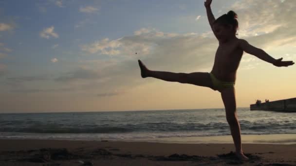 Liten flicka gör cartwheel på stranden på den vackra solnedgången. Siluett — Stockvideo