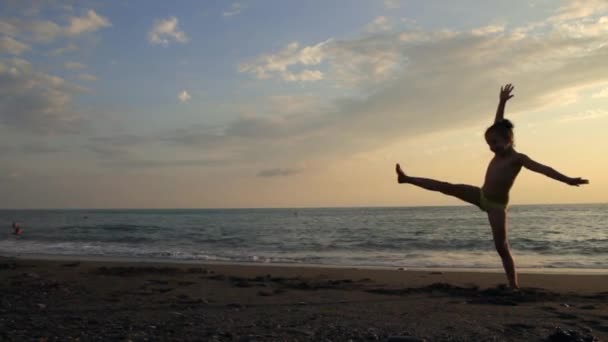 Kleines Mädchen, das am Strand am wunderschönen Sonnenuntergang Wagenrad fährt. Silhouette — Stockvideo