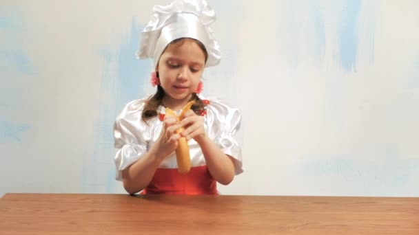 Menina de terno e chapéu do chef remove a pele de uma banana — Vídeo de Stock