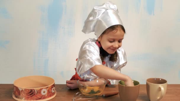 Девушка в шляпе шеф-повара облизывает палец и наливает сахар в миску с сырым яйцом . — стоковое видео